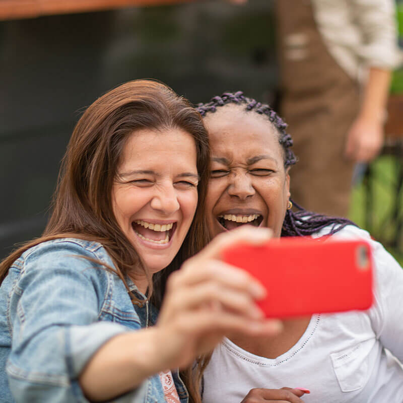 Two happy individuals smiling while posing together and capturing a self-portrait with their mobile device.